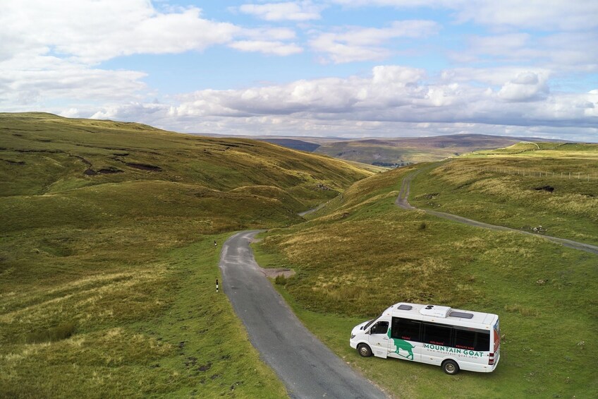 A white bus parked on a grassy hill with a winding road. 2
