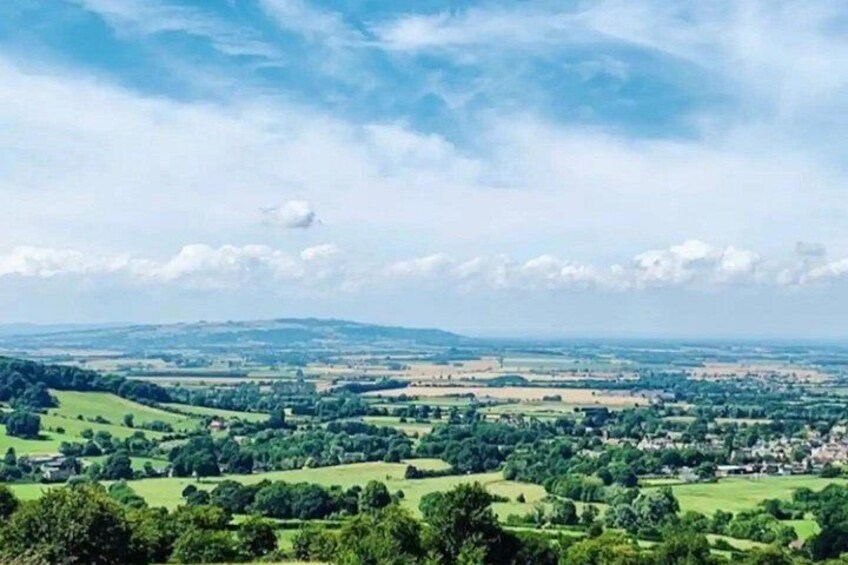 A rural landscape with rolling hills, scattered trees, and a distant village. 2