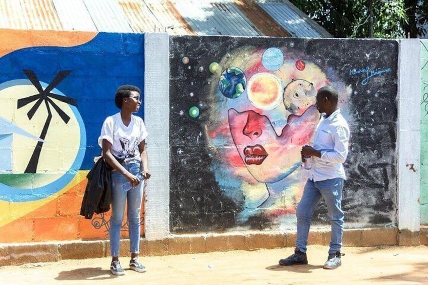 Two people standing in front of a colorful mural with a palm tree and a cosmic scene. 3