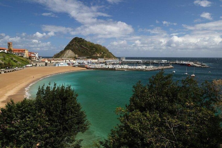 A coastal landscape with a sandy beach, a small hill, a pier, and boats. 1