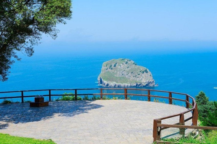 A coastal viewpoint with a wooden railing, a stone bench, and a clear view of the sea and a rocky island. 5