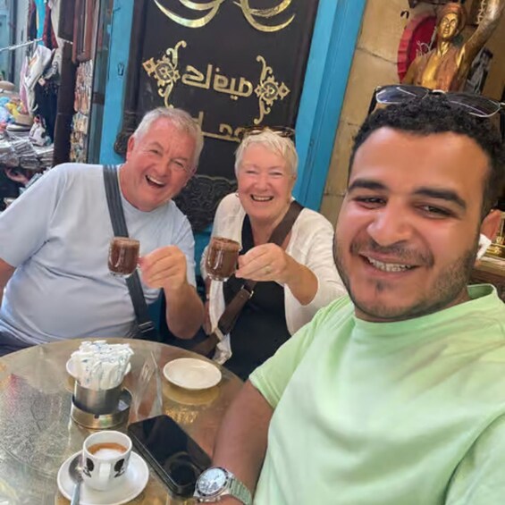 Tres personas brindando con bebidas en una mesa con tazas de café y un teléfono inteligente. 4