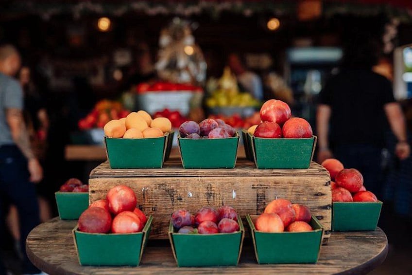 A wooden table with green baskets containing various fruits like apples and plums. 3