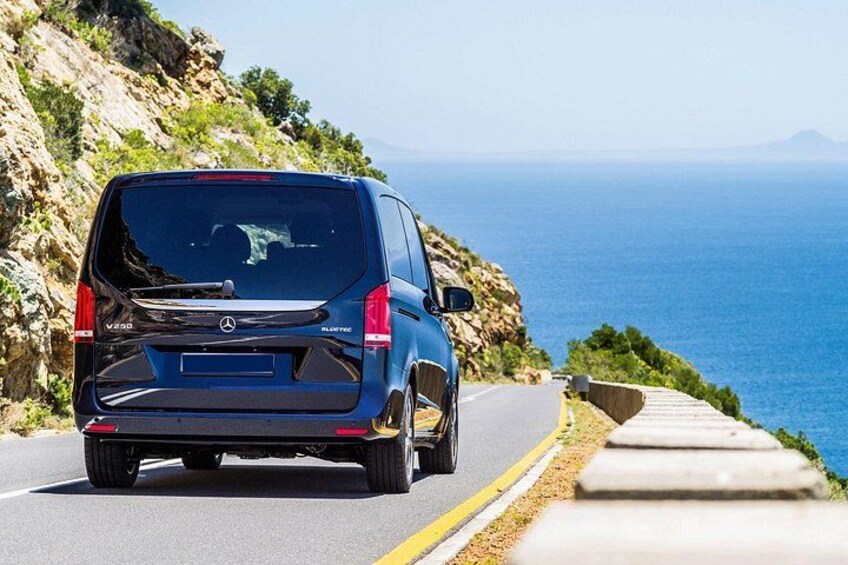 A blue Mercedes-Benz Sprinter van driving on a coastal road with a view of the sea and rocky cliffs. 3