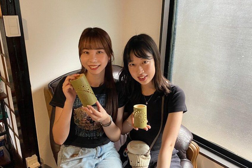 Two individuals sitting by a window, one holding a green cup and the other holding a yellow cup. 2