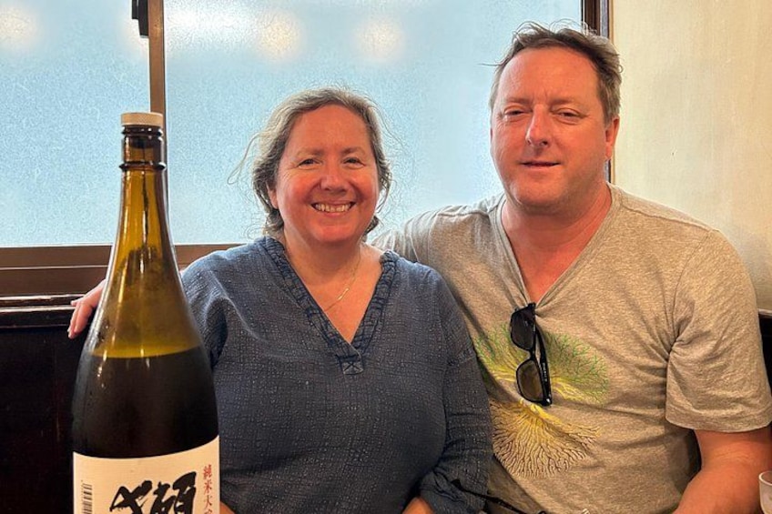 Two people sitting at a table with a bottle of wine. 2