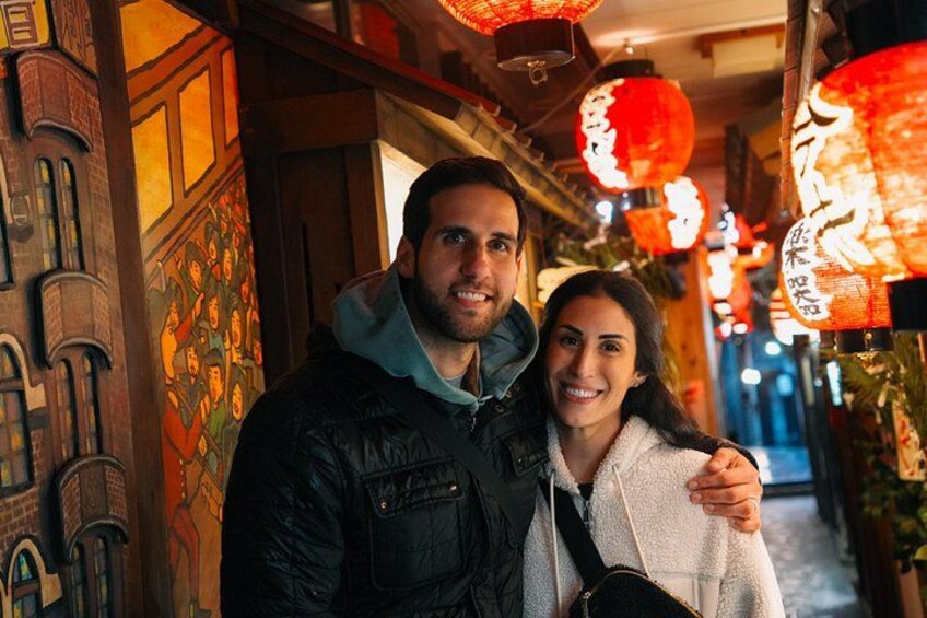A couple standing in a corridor with traditional red lanterns and a mural on the wall. 4