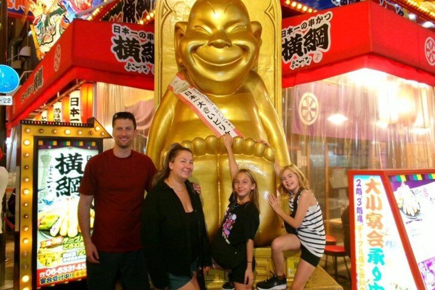 A large golden statue with Japanese text, a red and white sign, and a small illuminated display. 2