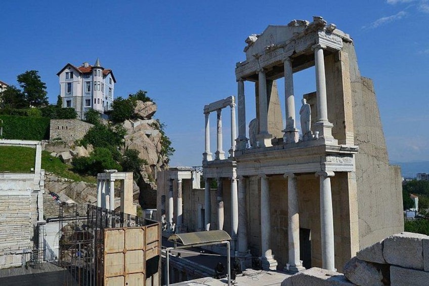 Ancient ruins with columns, a building on a hill, and a clear sky. 1