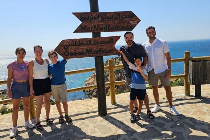 A group of people standing in front of a signpost with directions to Mer Mediterranee and Osea Atlantique. 1