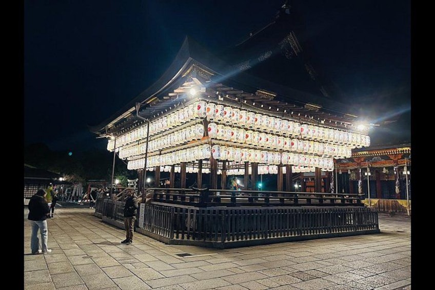 Ein traditionelles japanisches Gebäude bei Nacht mit beleuchteten Laternen, einem gefliesten Weg und einer Person in der Nähe. 2