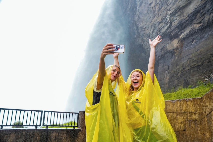 Two people in yellow rain ponchos taking a photo with a smartphone. 1