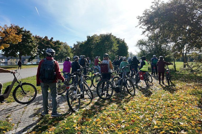 A group of cyclists on a paved path in a park with trees and grass. 5