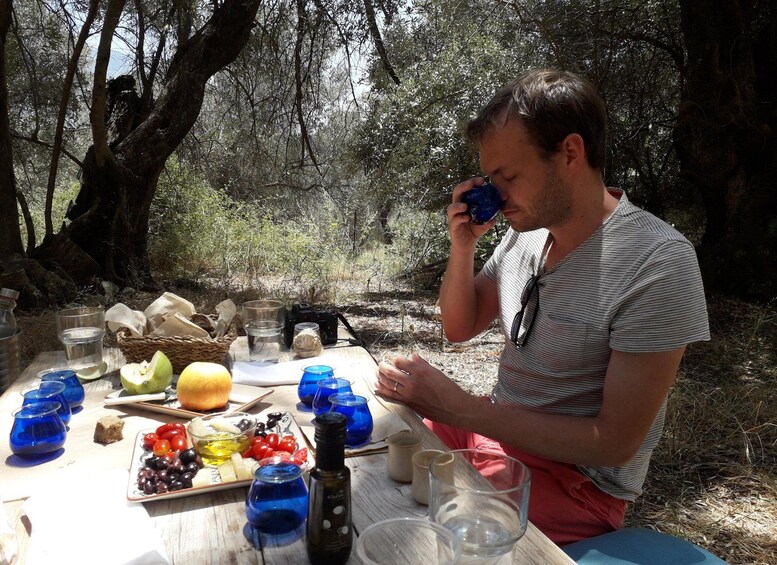A person sitting at a picnic table outdoors with food and drink items. 2