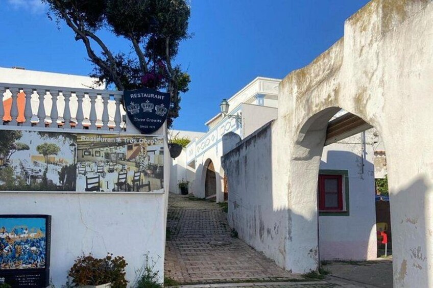 Una calle estrecha con un letrero de restaurante, una escalera y edificios blancos con arcos. 3