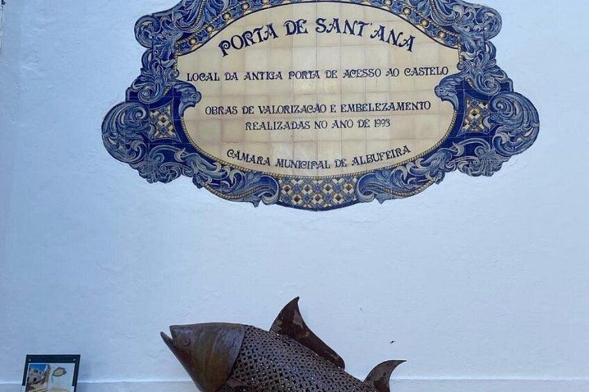 Una placa decorativa con detalles ornamentales en azul y oro, con texto en portugués. 5