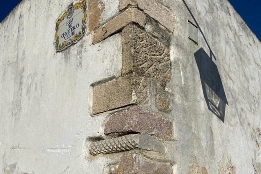 Una pared desgastada con una placa que dice 'Rua do Cemitério Velho' y la sombra de un farol. 4