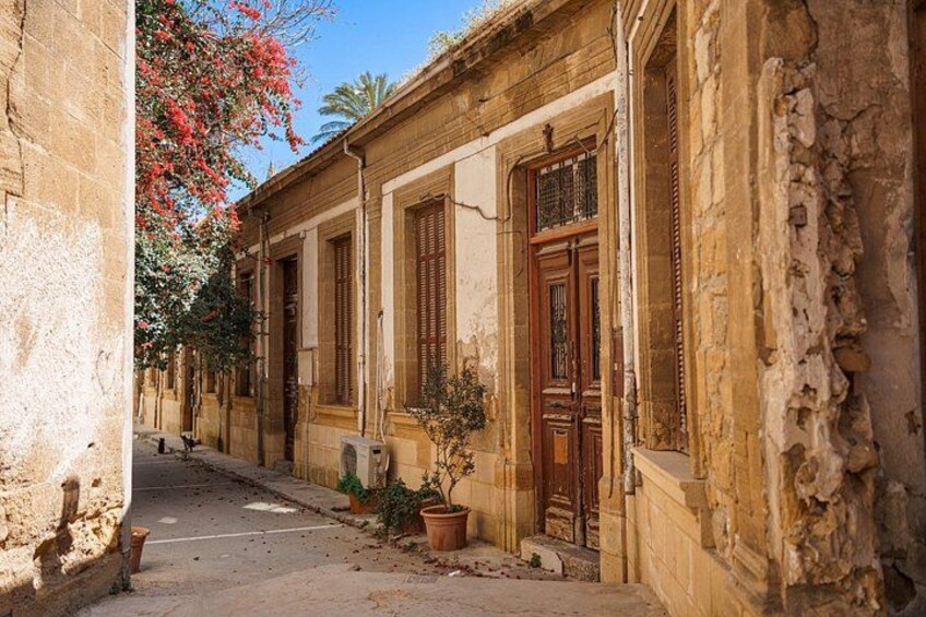 Una calle estrecha con edificios antiguos, puertas de madera y macetas con plantas. 4