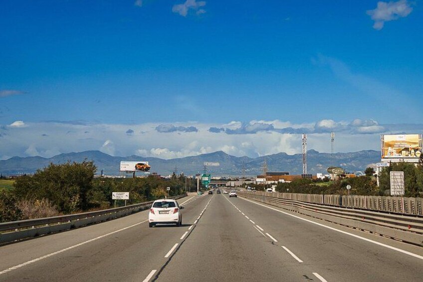 Una autopista con varios carriles, vehículos, vallas publicitarias y montañas distantes bajo un cielo despejado. 5