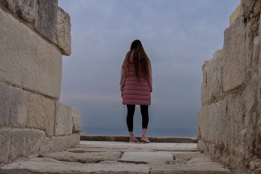 Una persona de pie entre muros de piedra, con vista al mar. 4