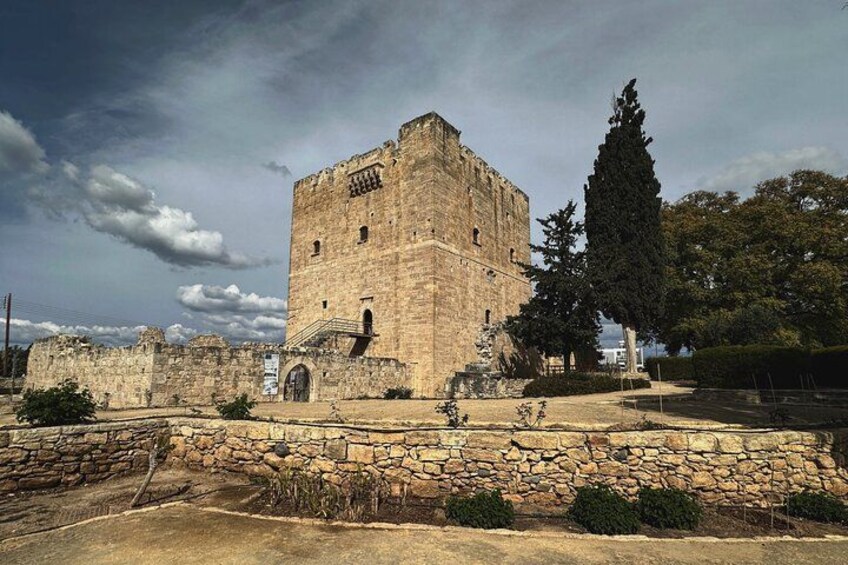 En historisk bygning i sten med et tårn, omgivet af en stenvæg og træer. 4
