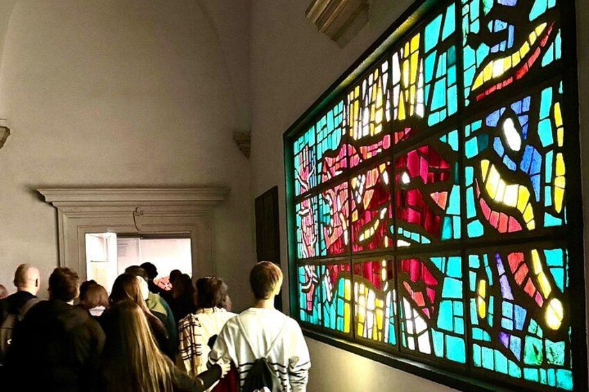 Un gruppo di persone all'interno di un edificio con un'ampia vetrata istoriata. 2