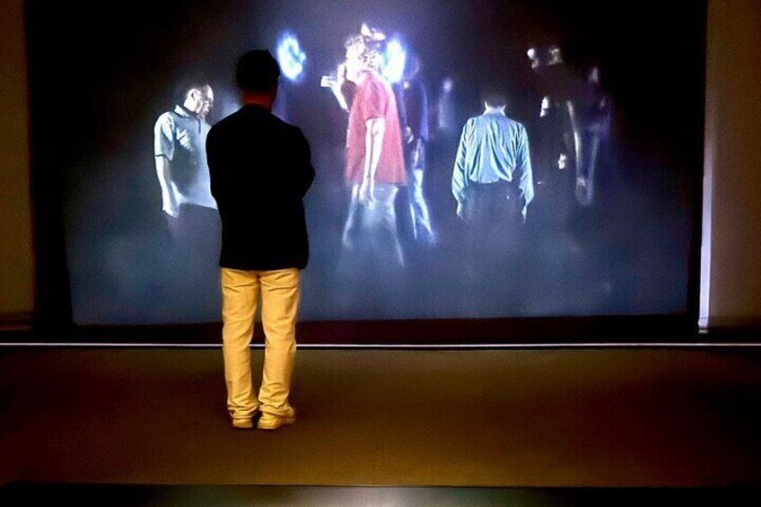 A person standing in front of a large screen displaying a group of people. 4
