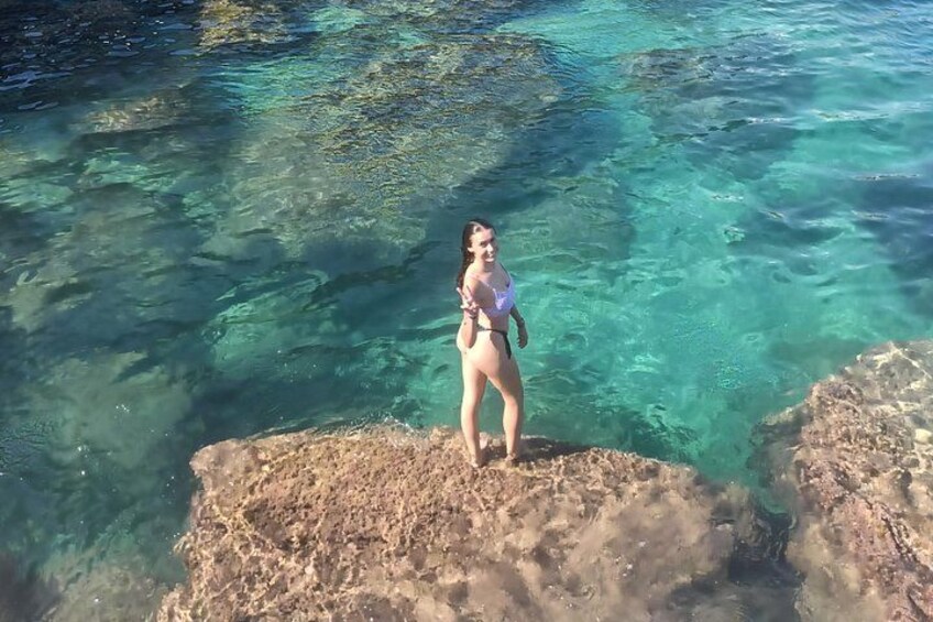 Une personne se tient debout sur un promontoire rocheux, au bord d’une eau d’un bleu limpide. 2