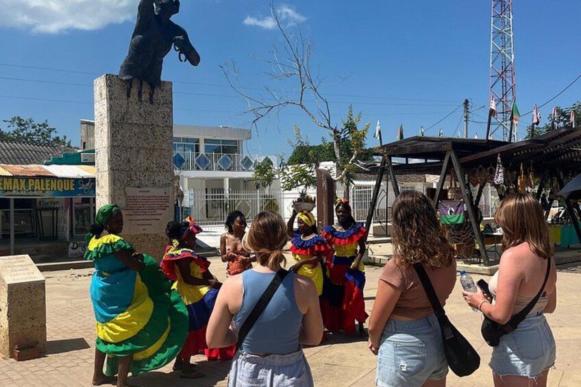 Una estatua de un caballo, un grupo de personas con trajes coloridos y un edificio con señalización. 2