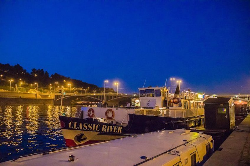 Een boot genaamd 'Classic River' aanmerkt bij een steiger, met een brug op de achtergrond. 3