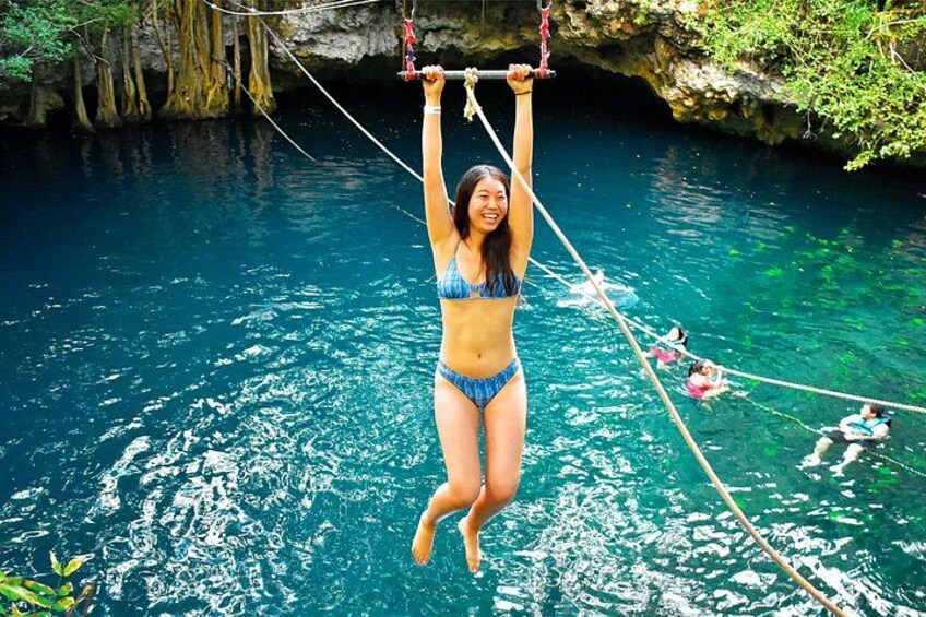 A person in a bikini suspended by ropes over clear blue water, with a rocky cave background. 3