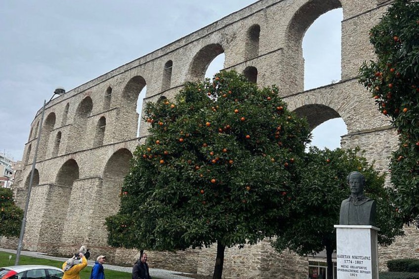 A historical stone aqueduct with arches, a tree with orange fruits, and a statue. 3