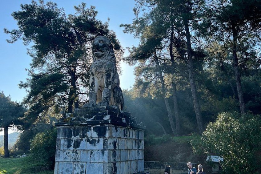 A weathered statue of a lion on a pedestal, surrounded by trees and greenery. 2