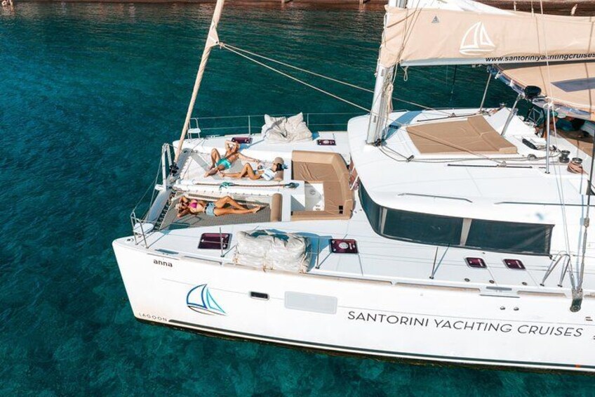 A white yacht named 'anna' with 'SANTORINI YACHTING CRUISES' branding, anchored in clear blue water. 1