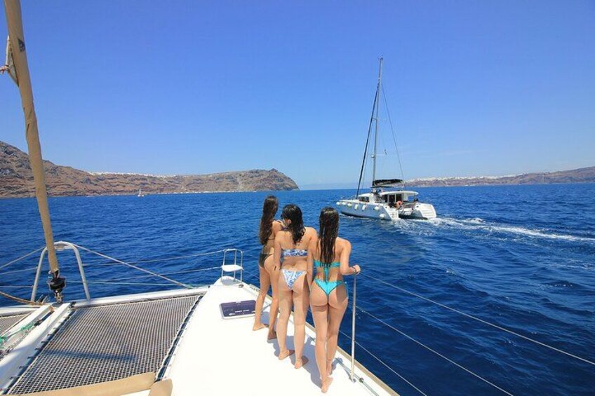 A sailboat with three people in swimsuits on the deck, a clear blue sea, and a distant coastline. 5