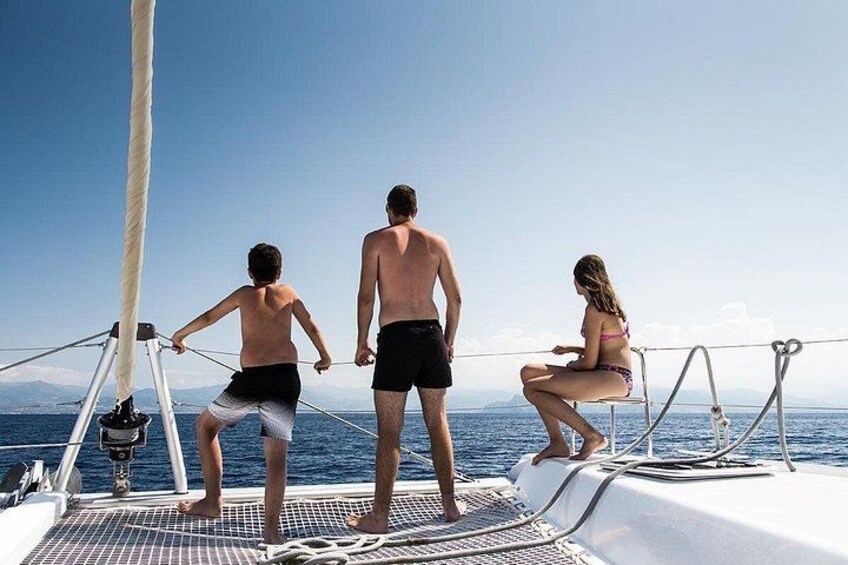 Three people on a sailboat, with a clear view of the ocean and distant mountains. 2