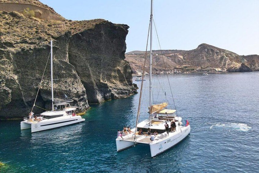 Two sailboats anchored near rocky cliffs in a calm sea. 2