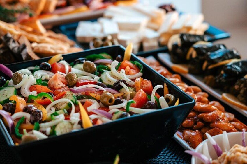 A variety of food items including a salad with vegetables and olives, and other dishes in the background. 2