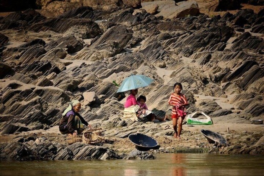 A rocky shoreline with people sitting and standing, some with bags and a child. 4