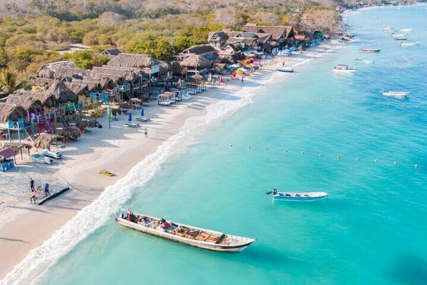 A beach with thatched-roof huts, a sandy shore, and several boats in the water. 2