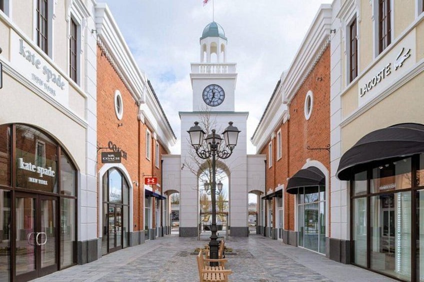 A shopping mall with a central clock tower, storefronts, and a cobblestone walkway. 2