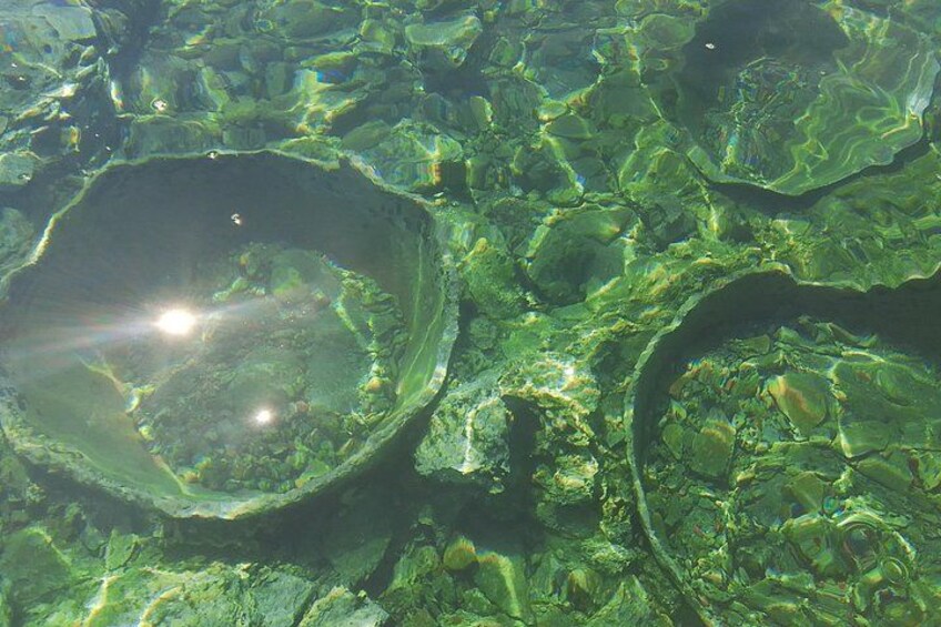Une vue sous-marine dégagée d’un paysage rocheux, avec des formations circulaires et la lumière du soleil filtrant à travers l’eau. 1