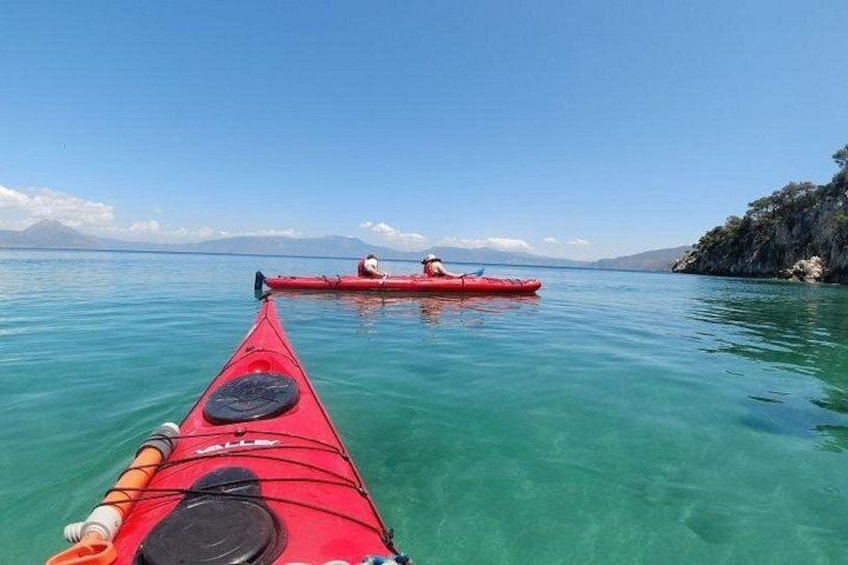 Un kayak rouge sur une eau calme, offrant une vue dégagée sur la côte et les montagnes lointaines. 3