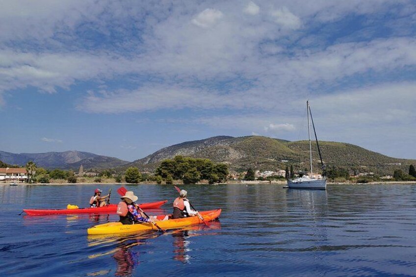 Un groupe de personnes fait du kayak sur un lac paisible, avec un voilier en arrière-plan et des collines à l’horizon. 2
