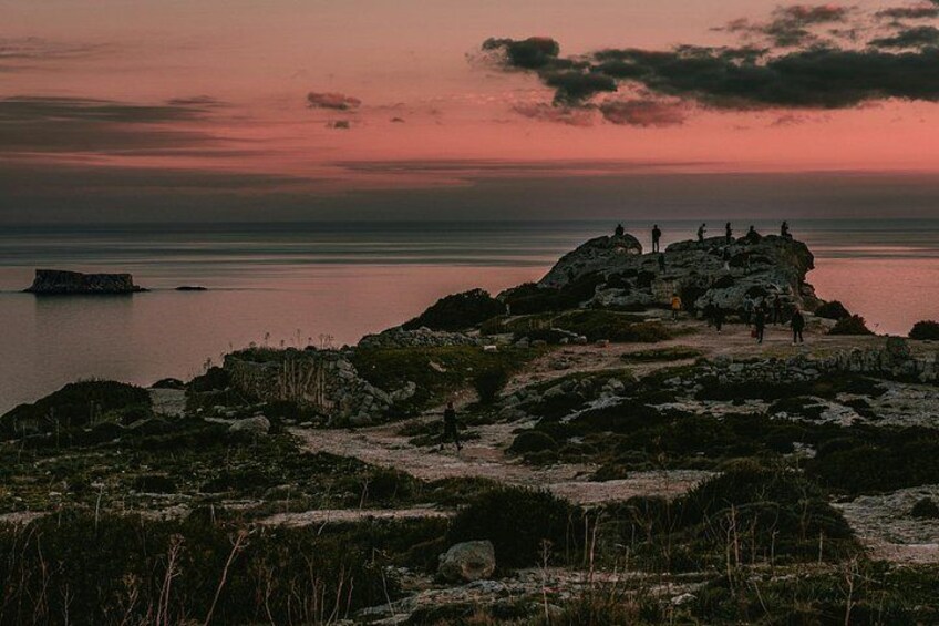 En klippefyldt kystlinje med mennesker, der går og står på klipperne i solnedgangen. 3