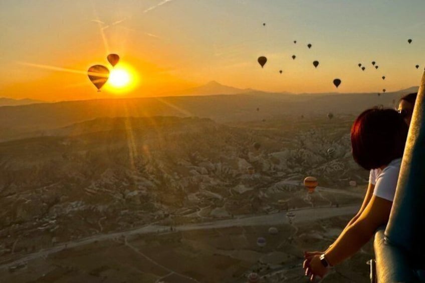 Una persona che guarda un paesaggio con mongolfiere e il sole al tramonto. 5