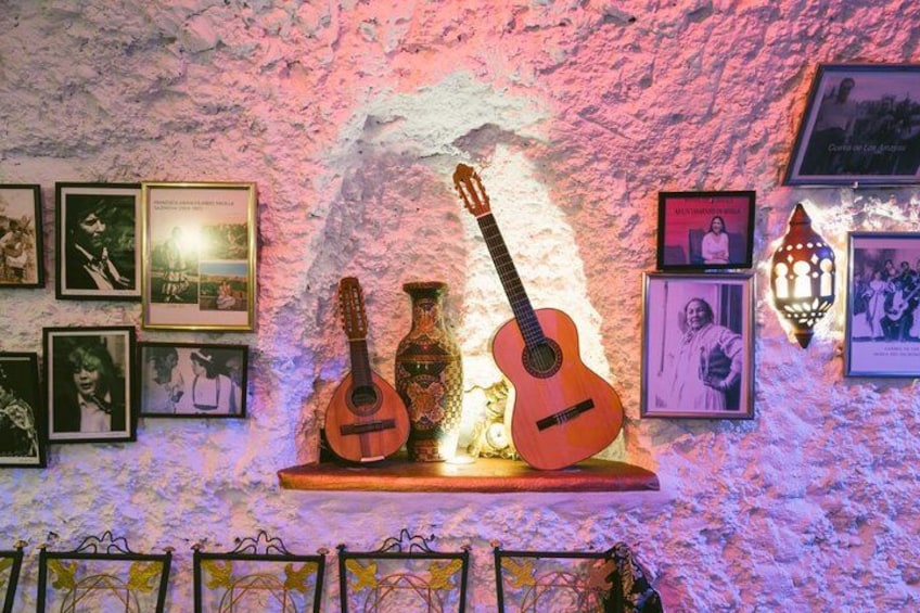 Una pared rústica con fotos enmarcadas, una guitarra y un florero. 4