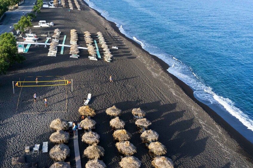 En strand med parasoller av halmtak, solstolar och ett volleybollnät. 5