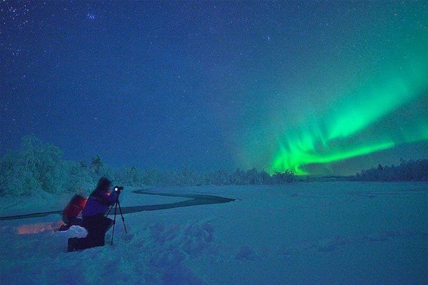 A person observing the Northern Lights with a telescope in a snowy landscape. 5