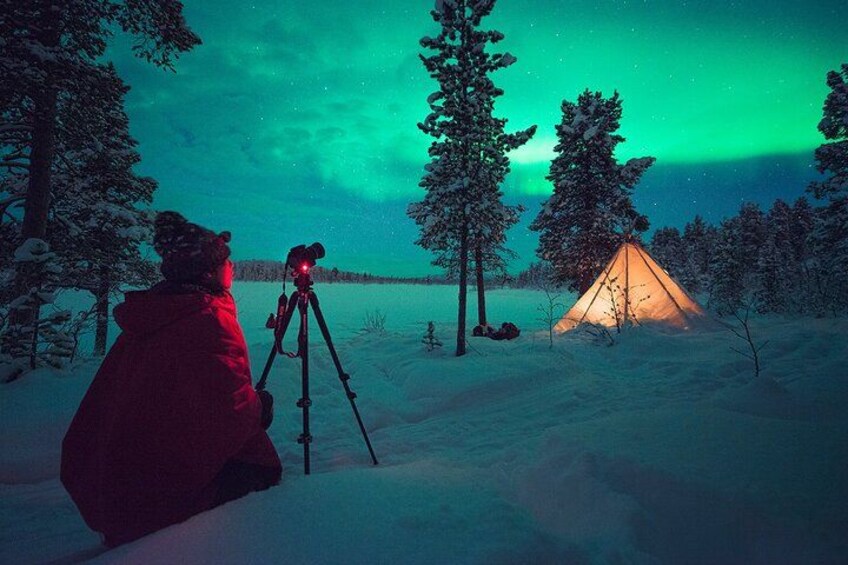En person med en kamera på ett stativ, ett tält och ett snöigt landskap med träd. 1